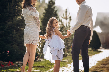 Family mother, father and daughter are beautiful and happy together, in white clothes, on a walkの写真素材