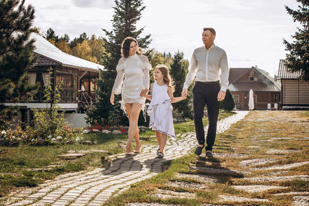 Family mother, father and daughter are beautiful and happy together, in white clothes, on a walkの写真素材