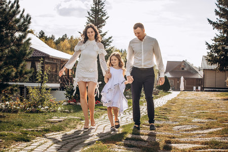 Family mother, father and daughter are beautiful and happy together, in white clothes, on a walkの写真素材