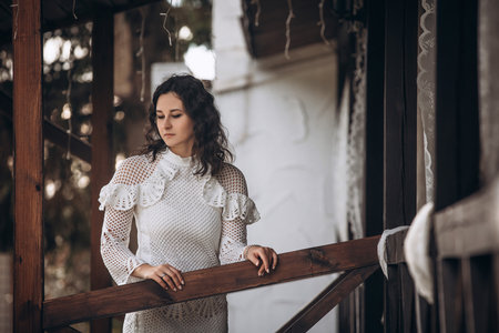 Beautiful young brunette woman in a white dress on the veranda of the houseの写真素材