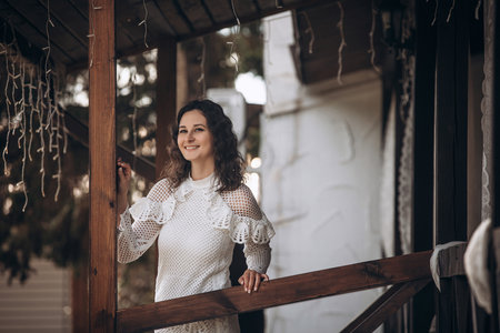 Beautiful young brunette woman in a white dress on the veranda of the houseの写真素材