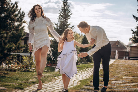 Family mother, father and daughter are beautiful and happy together, in white clothes, on a walkの写真素材