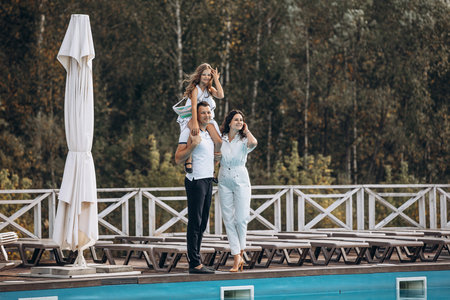 Family mother, father and daughter are beautiful and happy together, in white clothes, on a walk by the poolの写真素材