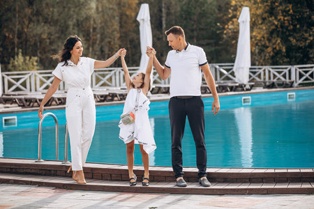 Family mother, father and daughter are beautiful and happy together, in white clothes, on a walk by the poolの写真素材