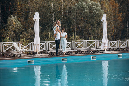 Family mother, father and daughter are beautiful and happy together, in white clothes, on a walk by the poolの写真素材