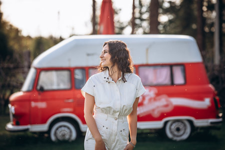 Beautiful young brunette woman in a white jumpsuit, at the red trailer busの写真素材