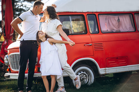 Family mother, father and daughter are beautiful and happy together, in white clothes, at the red trailer busの写真素材