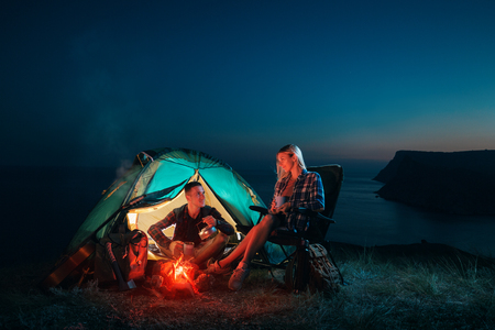 Young couple backpackers enjoying in the camping at night near the campfire. Romantic family Campsite. Happy man and woman hiking in the mountains.の写真素材