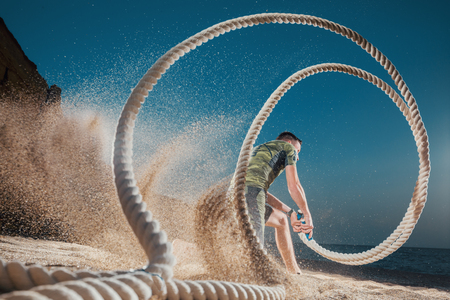 Man training with battle rope on the beach. Athlete doing cross fitness workout outdoor. Sport fit exercise.の写真素材