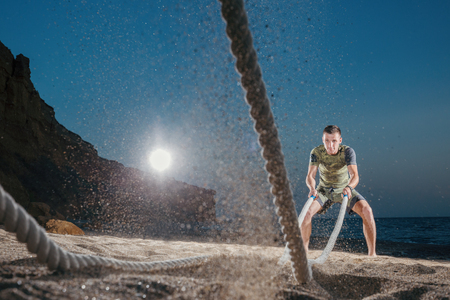 Man training with battle rope on the beach. Athlete doing cross fitness workout outdoor. Sport fit exercise.の写真素材