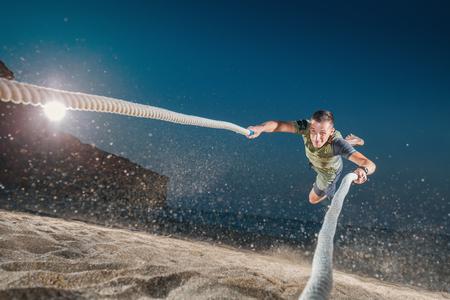 Young Man with battle ropes exercise on the beach. Cross Fitness on the sand in night.の写真素材
