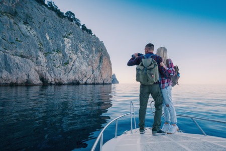 Adventures of a young couple on a yacht in the sea. Attractive man and woman backpackers travel by boat in the ocean near the mountains.の写真素材