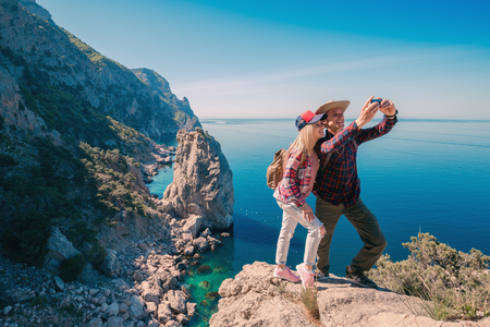 Young couple hikers taking selfie photo on phone in the mountains background the sea. Beautiful Man and Woman traveling active adventure vacations.の写真素材