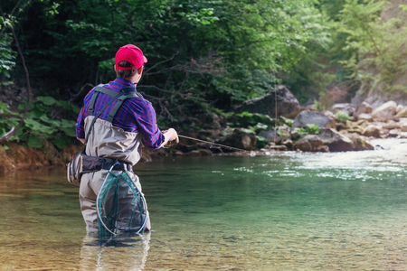 Fisherman catches a fish in the river with fly fishing. Catching trout and bass in the stream. Healthy lifestyle.の写真素材