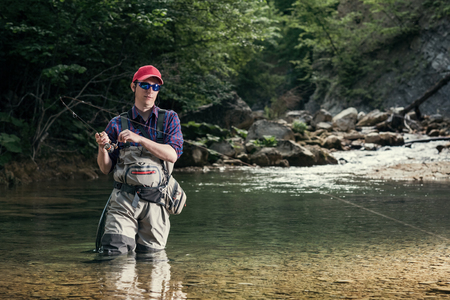 Fisherman catches a fish in the river with fly fishing. Catching trout and bass in the stream. Healthy lifestyle.の写真素材