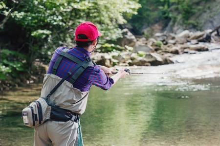 Man fisherman catching trout in the river fishing rod. Fly fishing in a forest creek in Europe. Professional sport angler catches a fish.の写真素材