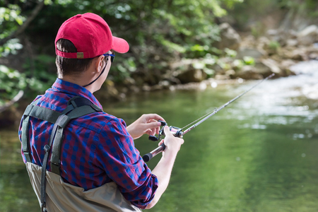 Man fisherman catching trout in the river fishing rod. Fly fishing in a forest creek in Europe. Professional sport angler catches a fish.の写真素材
