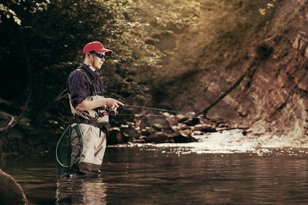 Fisherman catches a fish in the river with fly fishing. Catching trout and bass in the stream. Healthy lifestyle.の写真素材