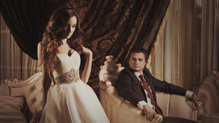 Bride and groom in a luxurious room in retro style. The rich young couple of man in suits and woman in vintage wedding dress.の写真素材