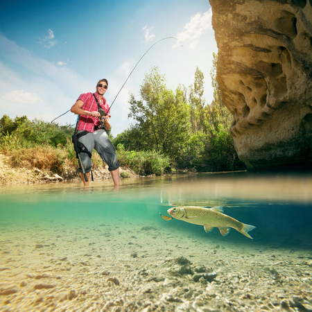 Fishing on the river. Young fisherman catches a fish. Fish closeup underwater.の写真素材
