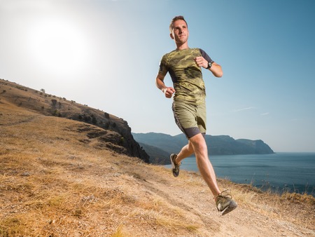 Man running on the mountain path. Happy runner jogging on country road. Athletic fit young sport fitness model in his twenties in full body length on trail outside in nature. Healthy lifestyle.の写真素材