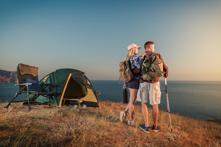 Happy young couple at campsite tent enjoying seaside. Man and woman camp on summer outdoor adventure hiking trip in mountain.の写真素材