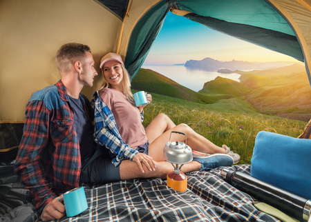 Happy couple in a tent drinking tea and enjoying mountain landscape at the sunset.の写真素材