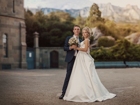 Wedding couple posing in the ancient city. Young cute bride with a bouquet of flowers and the groom embrace.
