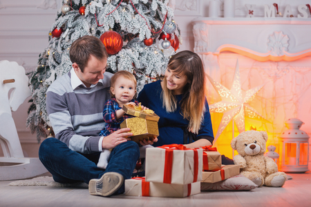 Merry Christmas celebration. Happy family mother father and baby at christmas tree with Xmas gifts at home.の写真素材