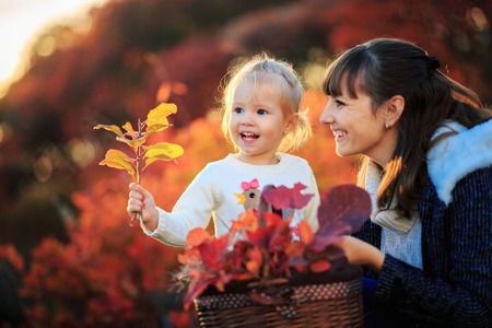 Mother and daughter with fallen leaves in autumn park. Little girl and her mom playing in the garden. - Imageの写真素材