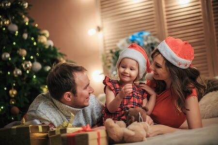 Christmas concept. Young Family Open Present Gift Bag, Looking to Magic Light. Young parents with children in red Santa hats celebrating Xmas at home.の写真素材
