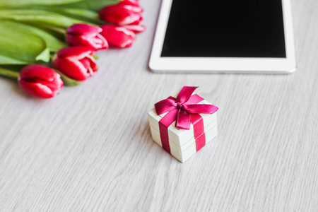 Red tulips, gift box with a red bow and tabletの写真素材