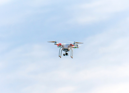 drone quad copter with high resolution digital camera flying hovering in the blue sky.