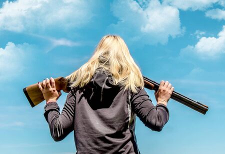 Young girl with blond hair with a weapon for shooting at flying targets against the sky with cloudsの写真素材
