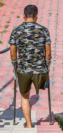 Man with an amputated leg on crutches in nature in the cityの写真素材