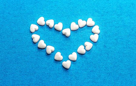 White dragee in the shape of a heart on a blue background. Beautiful background of hearts. The...