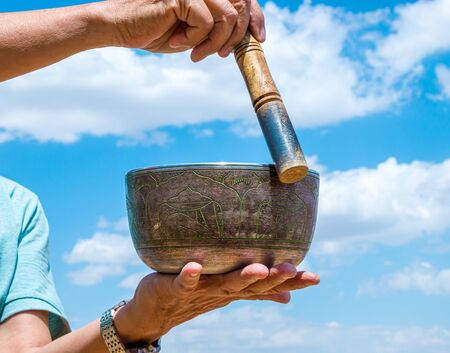 A man plays the National musical instrument Tibetan singing bowl against the sky close-upの写真素材