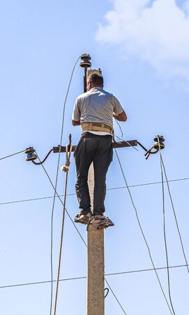 A man on a concrete pole mounts wires against the sky.の写真素材