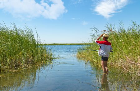 Fisherman with fishing rod in the reeds by the lake landscapeの写真素材