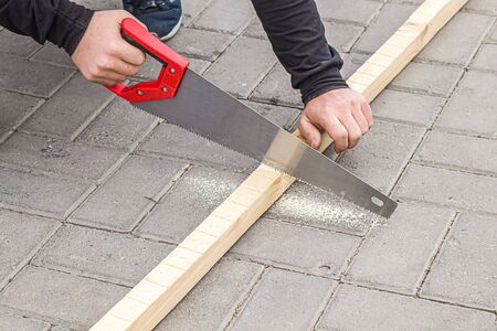 Man sawing a wooden block with a hand sawの写真素材