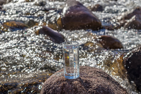 Glass cup with cold water on a background of a mountain river.の写真素材