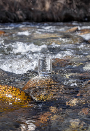 Glass cup with cold water on a background of a mountain river.の写真素材