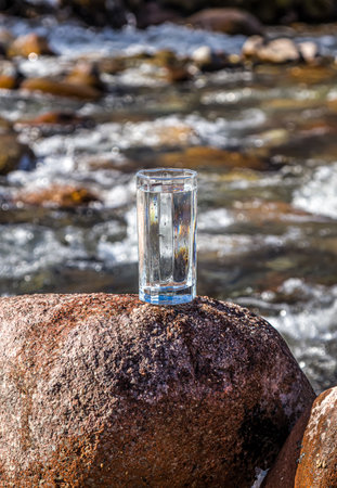 Glass cup with cold water on a background of a mountain river.の写真素材