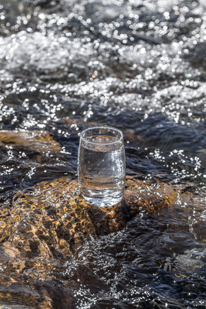 Glass cup with cold water on a background of a mountain river.の写真素材