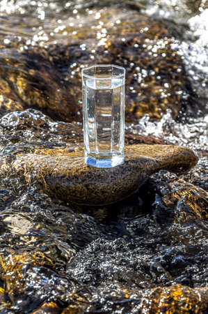 Glass cup with cold water on a background of a mountain river.の写真素材