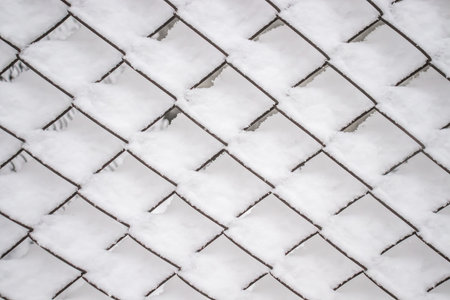 Metal fence made of mesh netting covered with snow in nature as a background.の写真素材
