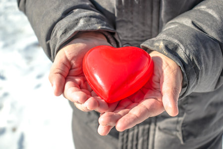 Red heart in the hands of a man on a background of snowの写真素材