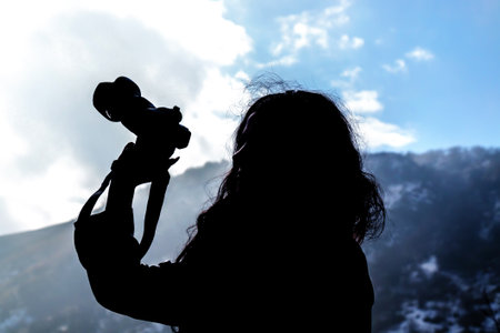 Silhouette of a girl photographer with a camera in the mountains against the skyの写真素材