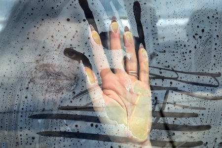 Misted glass of a car with a girl's hand on the glass. Request for help, depression, stressの写真素材