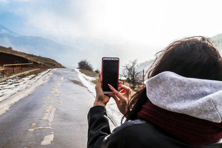 Phone in the hands of a photographer woman in the mountains against the skyの写真素材